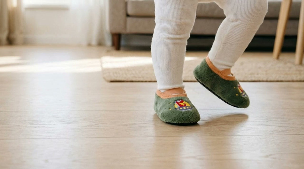 A toddler stepping across a wooden floor in green dinosaur grip socks
